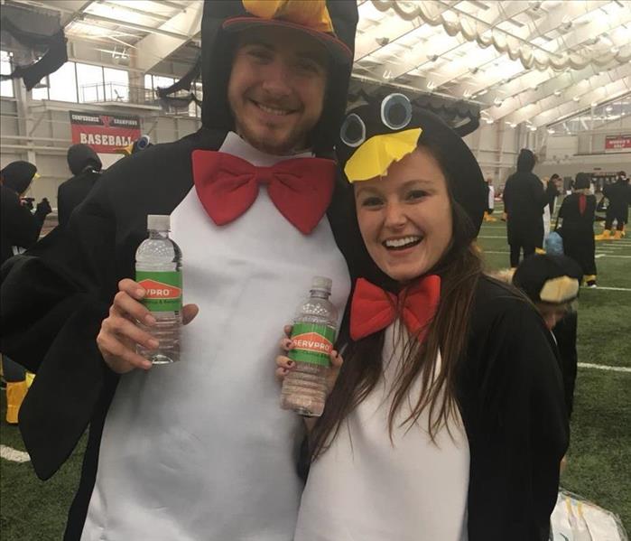 Two people dressed like penguins holding SERVPRO water bottles